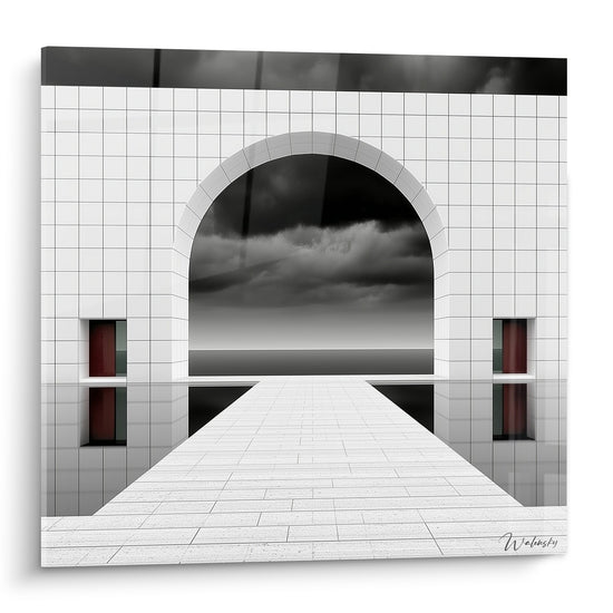 Arche blanche carrelée ouverte sur ciel anthracite orageux, allée pavée et reflets sur eau miroir